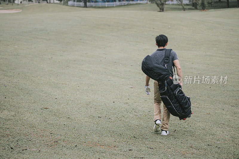 Asian chinese male golfer carrying golf bag walking on the golf course during rainy day